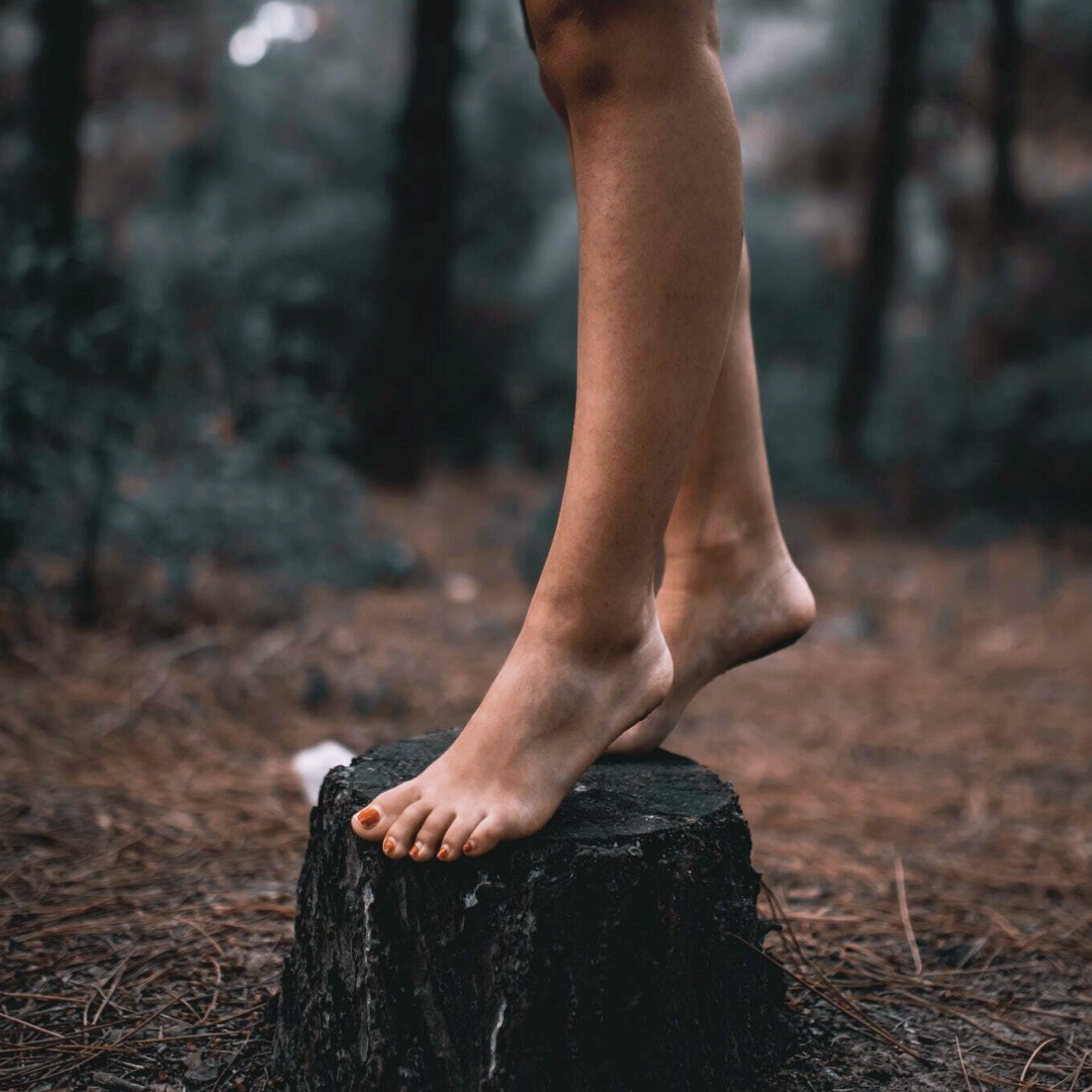 woman standing barefoot on a stump for an article about foot care in the summertime